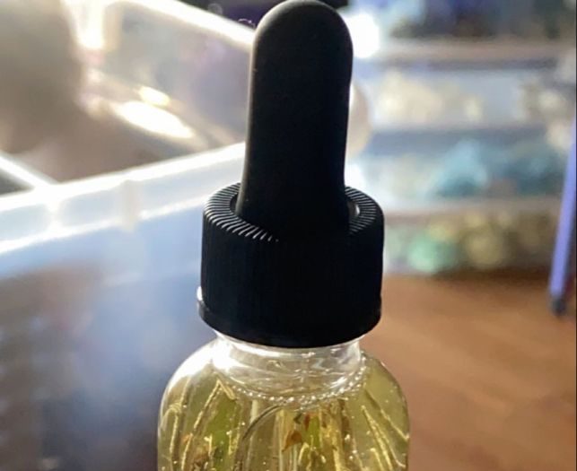 A glass dropper bottle of oil with herbs inside