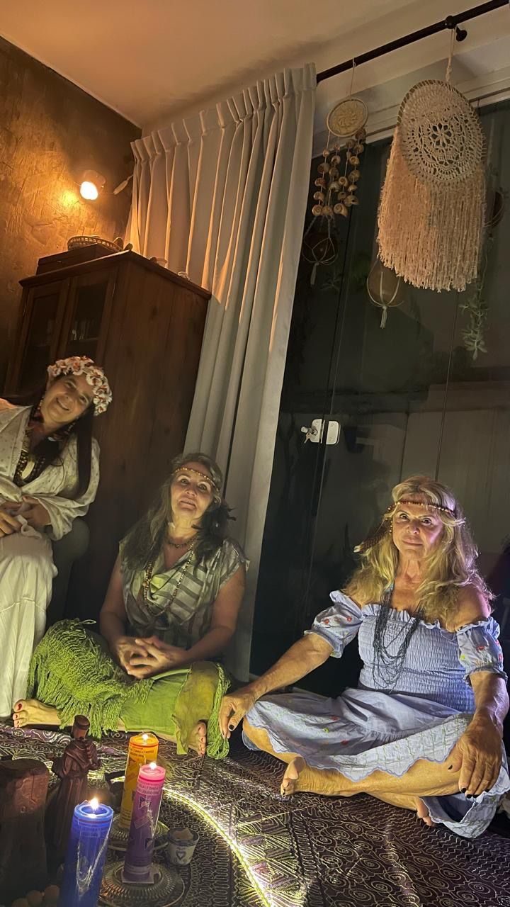 Three women seated together on the floor of a room lit by candles